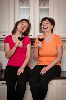 Happy senior mother with daughter talking and drinking wine at kitchen