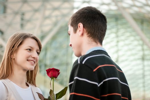 Young man handing over a flower (red rose) to woman - outdoor lifestyle scene