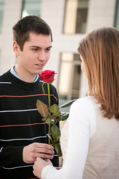 Young man handing over a flower (red rose) to woman - outdoor lifestyle scene