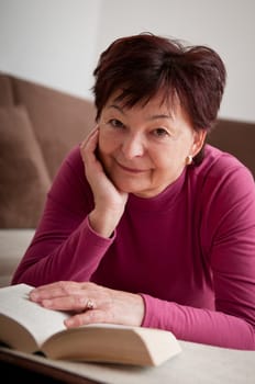 Smiling senior woman reading book at home on sofa