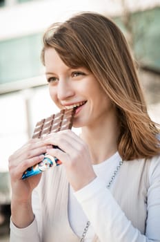 Lifestyle outdoor scene - young beautiful woman eating chocolate