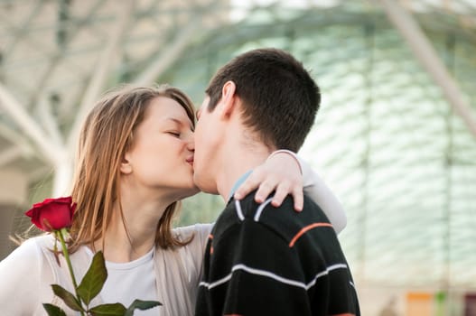Young man handing over a flower (red rose) to woman and kissing her