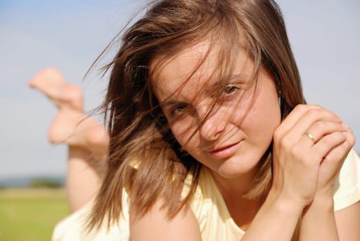 Young woman with sensual look lying in grass and wind blowns her hair into face