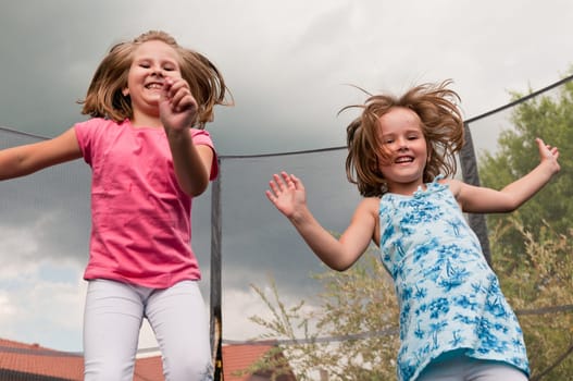Small cute children jumping on trampoline - garden and family house in background