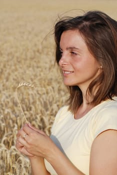 Young woman with wheat in hands with golden field background