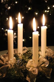 Christmas advent wreath with burning candles. Lights on x-mas tree in background