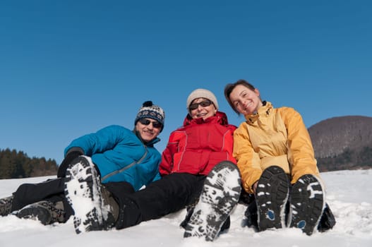 Family portrait - senior man and woman with their adult daughter in winter - sitting in snow