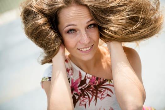 Outdoor portrait of young happy smiling woman playing with hair