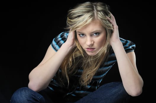 Young blond woman (teenager) in depression isolated on black background