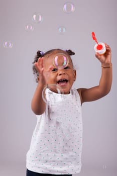 Cute little African American girl playing with soap bubbles