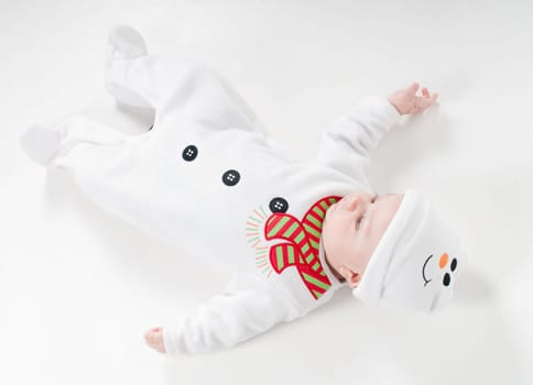 Baby boy in snowman costume lying on the floor on light background