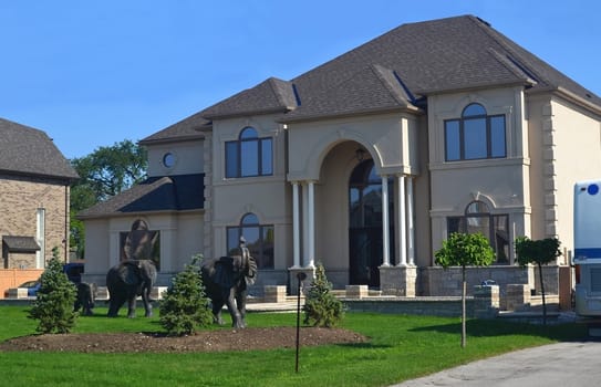 A beautiful new big house from the front with the front yard and the nice decoration with three bronze elephants and some small trees.
