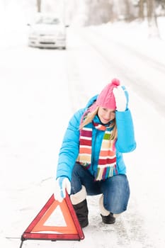 Woman putting reflector triangle car breakdown winter snow sign