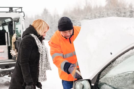 Woman mechanic looking under car hood snow assistance winter broken