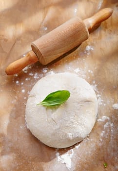 Mound of freshly kneaded dough sprinkled with flour left to rise alongside a wooden rolling pin on a wood countertop