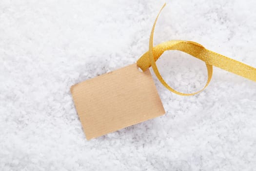 Blank paper gift label with a decorative golden ribbon on a bed of snow for your Christmas greeting