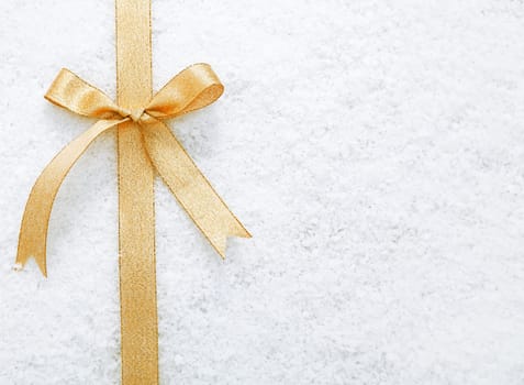 Decorative simple gold ribbon and bow on a background of winter snow with copyspace for your Christmas or festive greeting