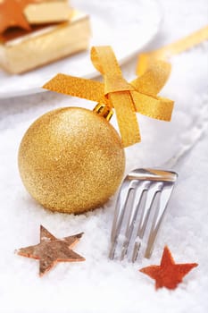 Golden Christmas Bauble with a bow and xmas stars and cutlery on snow background
