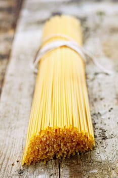 Bundle of uncooked Italian spaghetti lying on a textured old wooden surface with shallow dof and focus to the ends of the strands