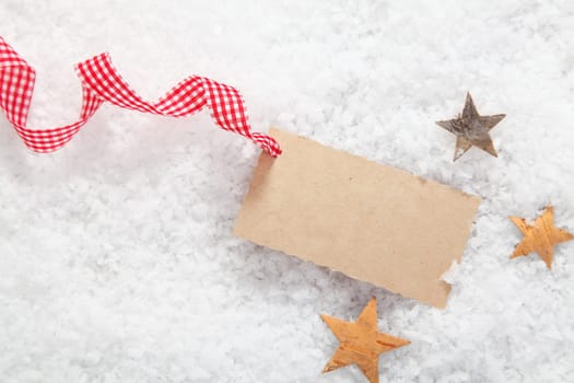 Blank Christmas gift label with a decorative red and white checked rustic ribbon surrounded by stars on fresh winter snow
