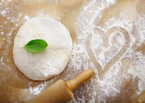 Ball of fresh dough left to rise alonside a scattering of flour with a handdrawn heart symbolic of preparing dinner for a date with love
