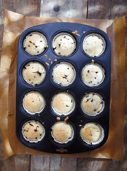 Overhead view of a baking tray with freshly baked muffins from the oven cooling on an old wooden surface