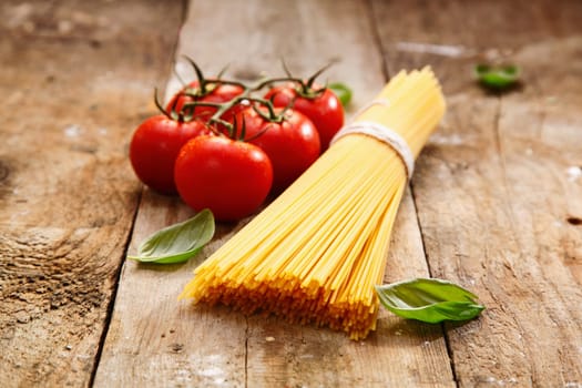 Bucnch of raw spaghetti with a truss of tomatoes in a rustic scene