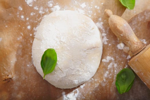 Fresh bread dough with a rolling pin on a wooden surface ready to be rolled out for a pizza base or pastry