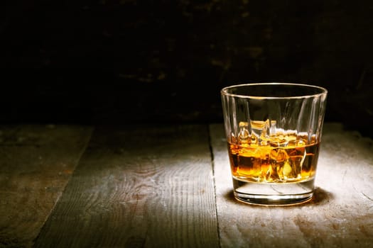 Scotch on wooden background with copyspace. An old and vintage countertop with highlight and a glass of hard liquor