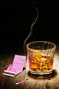 Call me invitation handwritten on a matchbook alongside a glass of brandy in a nightclub or bar with a burning match in the foreground
