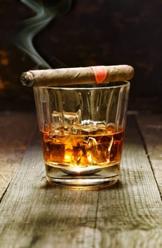 Burning Cuban cigar resting on a glass of brandy in a bar, the luxury pleasures of a wealthy macho man