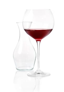 Glass of red wine with an empty glass carafeon a reflective white surface