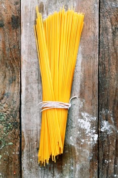 Bundle of Italian spahgetti pasta tied with string lying on old textured wooden boards with a scattering of flour