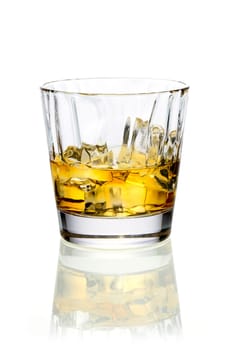 Glass of golden whiskey or brandy served on ice on a reflective white surface