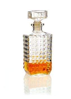 Stoppered whiskey or brandy decanter one third full of alcohol on a reflective white surface