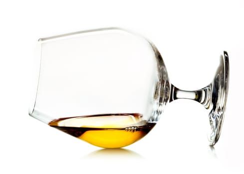 Glowing golden cognac or brandy in a snifter glass lying on its side on a white background