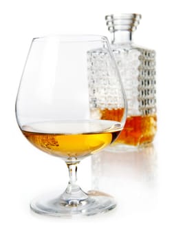 Aged golden brandy or cognac in a snifter with a cut glass decanter on a reflective white studio background