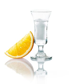 Shot glass with vodka or gin on the rocks served with a slice of fresh orange on a white studio background with reflection