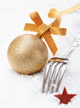 Shiny silver Christmas fork and ornamental gold glitter bauble with a star in soft white winter snow