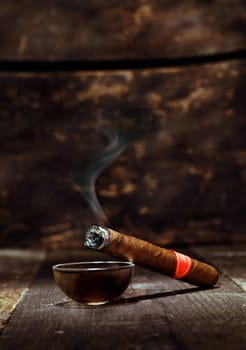 Burning handmade luxury Cuban cigar resting on an ashtray on an old wooden countertop in a nightclub or bar with copyspace