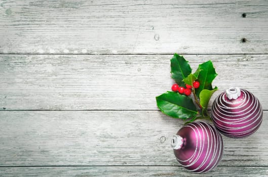 Christmas holly and pretty purple baubles with a spiral pattern on rustic wooden white painted boards with woodgrain texture and plenty of copyspace
