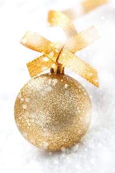 Glittering gold Christmas ball with an ornamental gold bow in winter snow with falling snowflakes