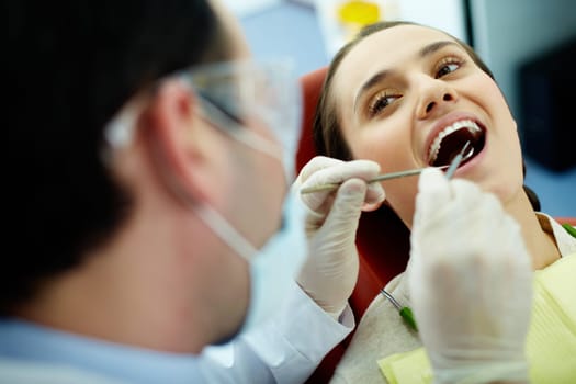 Smiling woman sitting in dentists chair while doctor examining her teeth