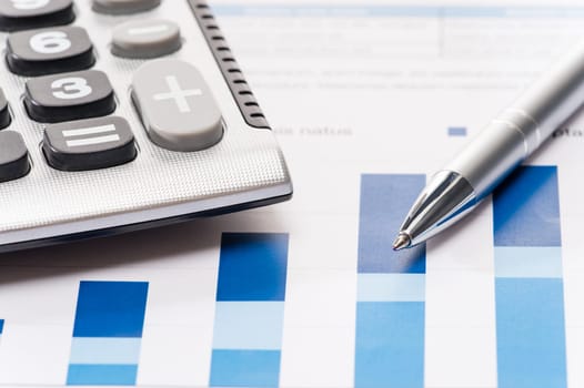 Business silver pen and calculator over office charts close-up