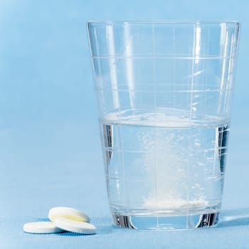Fizzy vitamin capsule throw in water glass on blue background