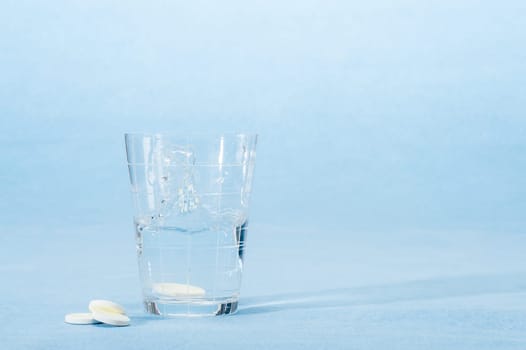 Fizzy vitamin capsule throw in water glass on blue background