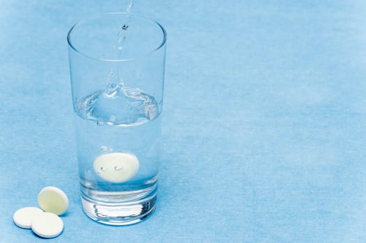Soluble tablet throw in water glass on blue background