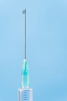 Medical syringe drop falling from needle on blue background