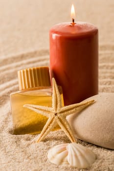 Spa setting candle with oil seashell star on sand