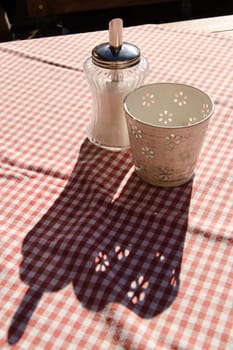 Sugar shaker on a red and white tablecloth in backlight